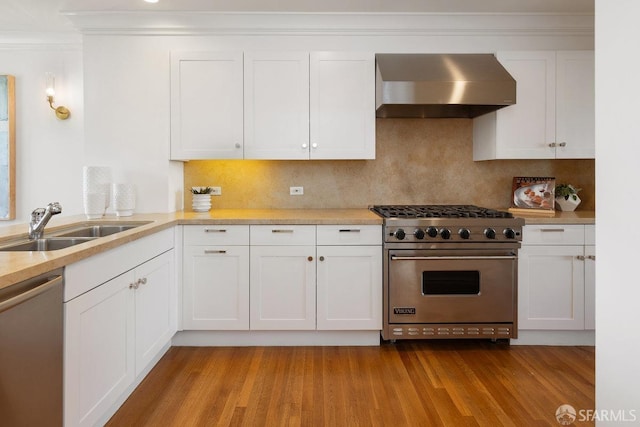 kitchen with a sink, white cabinets, light countertops, wall chimney range hood, and appliances with stainless steel finishes