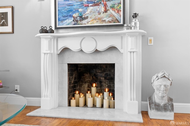 interior details with a warm lit fireplace, baseboards, and wood finished floors