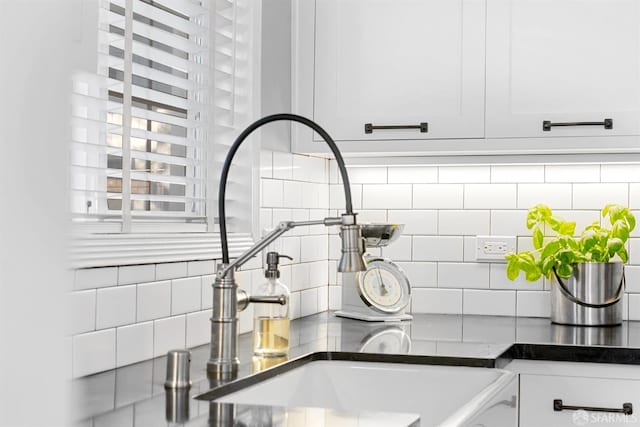 interior details featuring dark countertops, white cabinetry, a sink, and backsplash