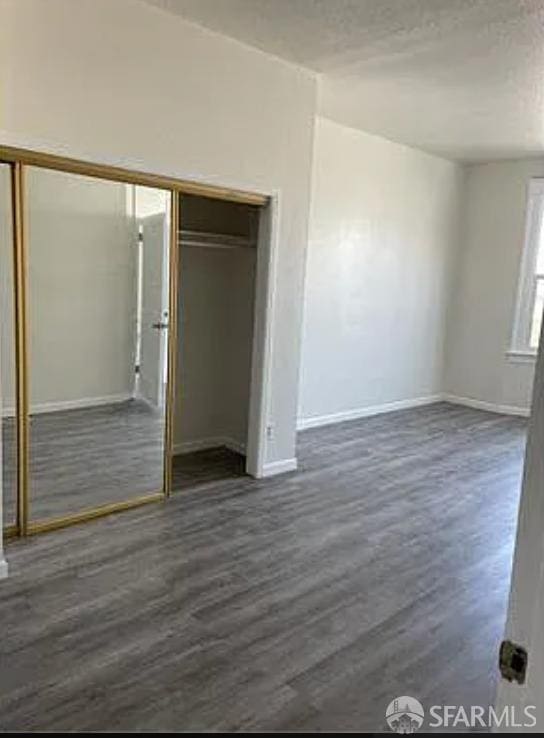 unfurnished bedroom featuring dark wood-style floors, a closet, baseboards, and a textured ceiling