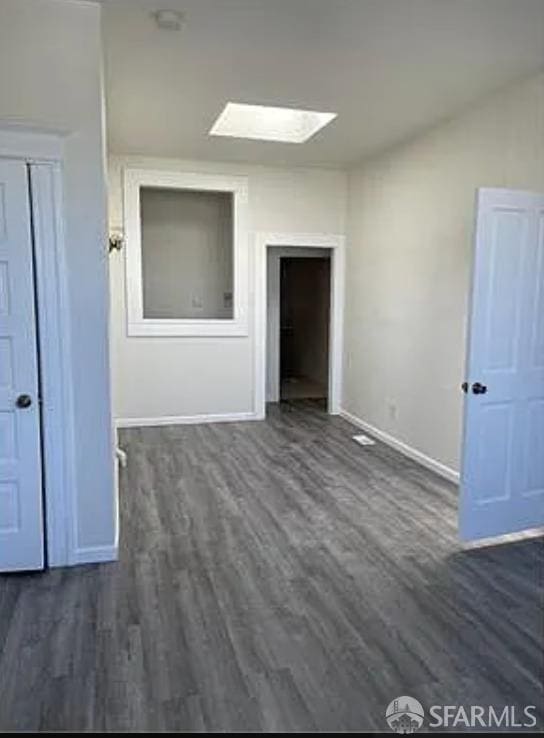 unfurnished room with dark wood-style floors, a skylight, and baseboards