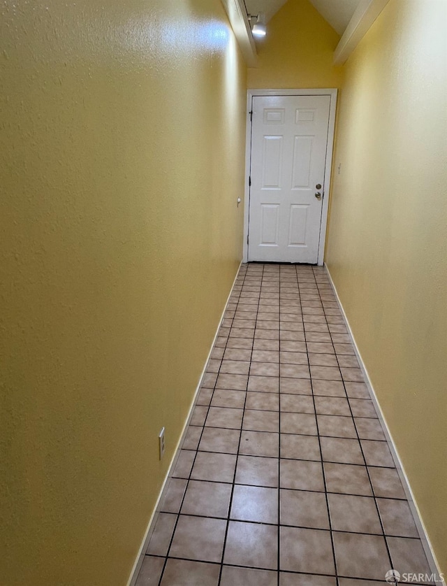 hall featuring light tile patterned flooring, baseboards, and vaulted ceiling
