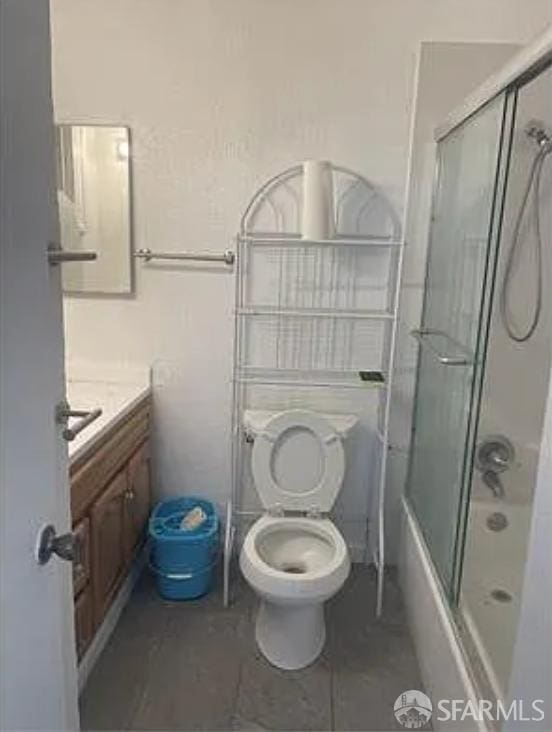 full bathroom with tile patterned floors, bath / shower combo with glass door, toilet, and vanity
