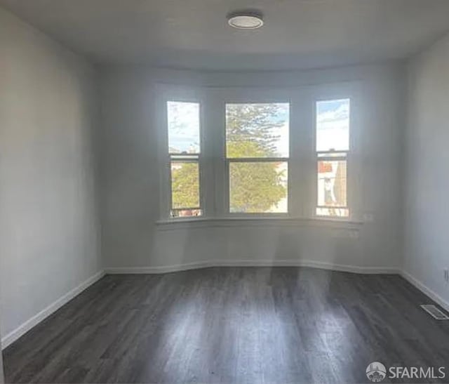 unfurnished room with wood finished floors, a wealth of natural light, and visible vents