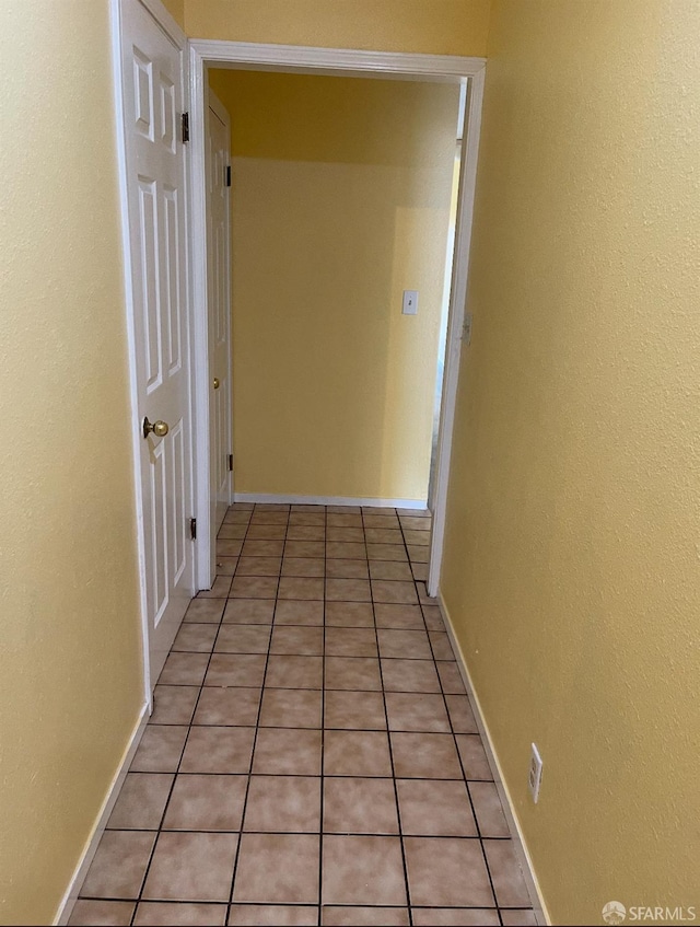 corridor featuring light tile patterned flooring and baseboards