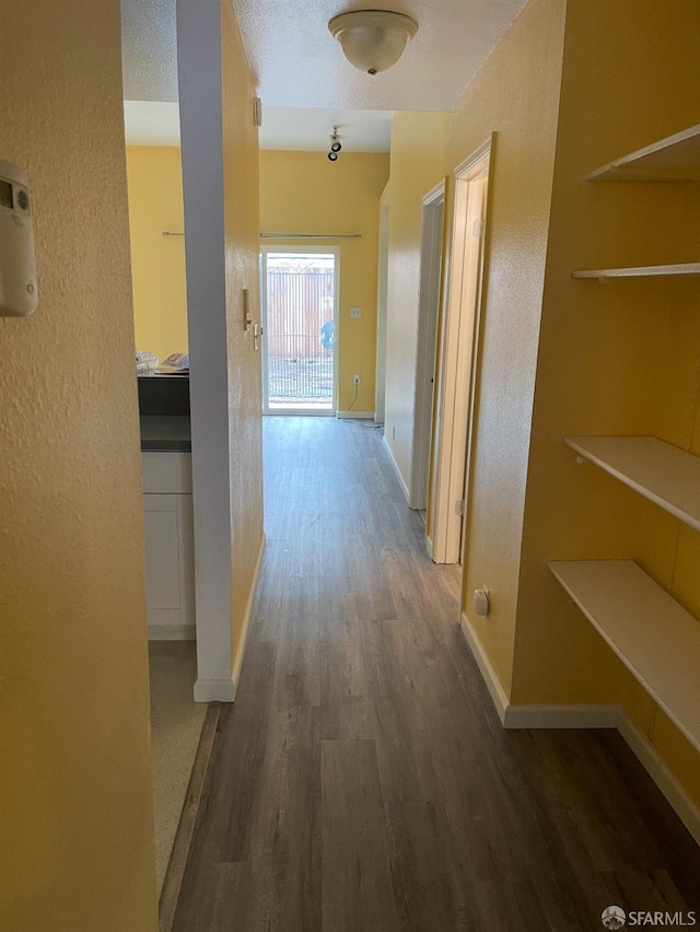 hallway featuring a textured wall, baseboards, and wood finished floors