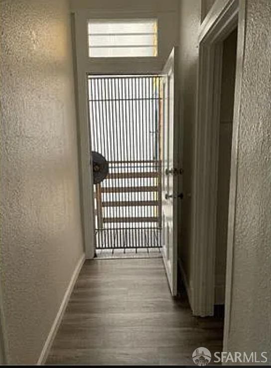 doorway to outside with baseboards, a textured wall, and wood finished floors
