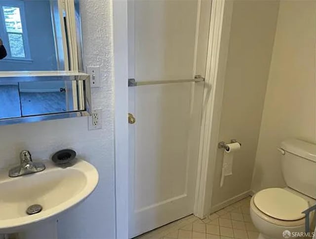 bathroom with toilet, a sink, and tile patterned flooring