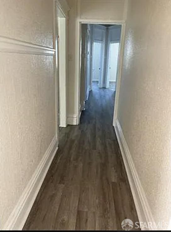 corridor with dark wood-style flooring and a textured wall