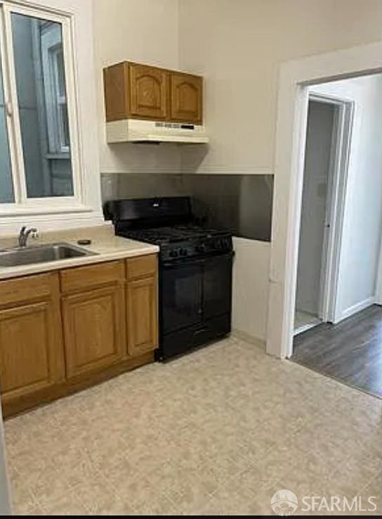 kitchen with black range with gas stovetop, light countertops, a sink, brown cabinets, and under cabinet range hood