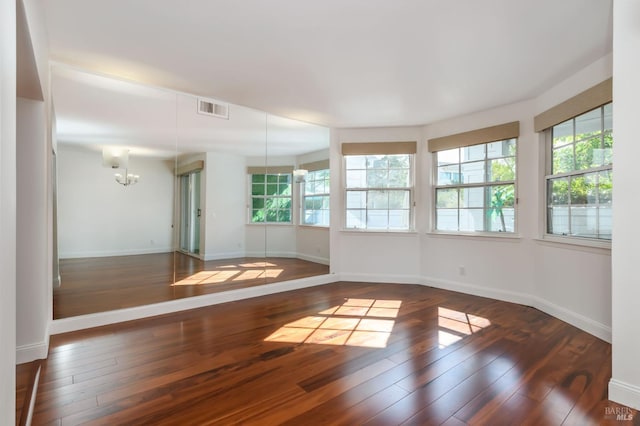 spare room featuring dark wood-style flooring, visible vents, baseboards, and an inviting chandelier