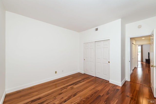 unfurnished bedroom with a closet, visible vents, baseboards, and wood finished floors