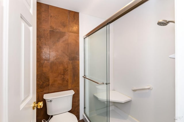 bathroom with toilet, a shower stall, and tile walls