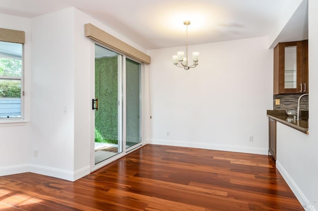 unfurnished dining area featuring a notable chandelier, baseboards, and dark wood-type flooring