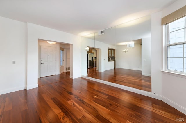 empty room with dark wood-style floors, a chandelier, visible vents, and baseboards