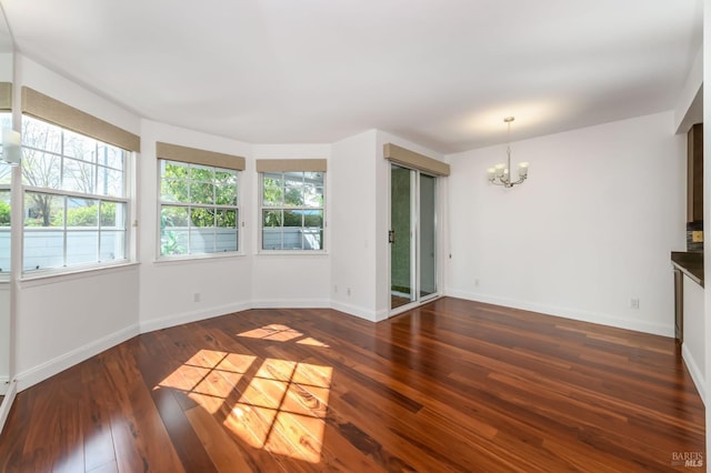 unfurnished living room featuring a healthy amount of sunlight, baseboards, a chandelier, and dark wood-style flooring