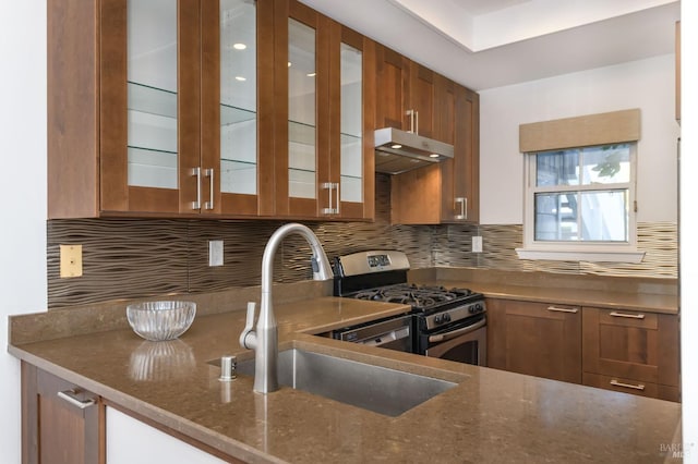 kitchen featuring tasteful backsplash, glass insert cabinets, stainless steel gas stove, a sink, and under cabinet range hood