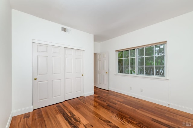 unfurnished bedroom with a closet, visible vents, baseboards, and wood finished floors