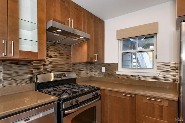 kitchen with appliances with stainless steel finishes, backsplash, brown cabinetry, and under cabinet range hood