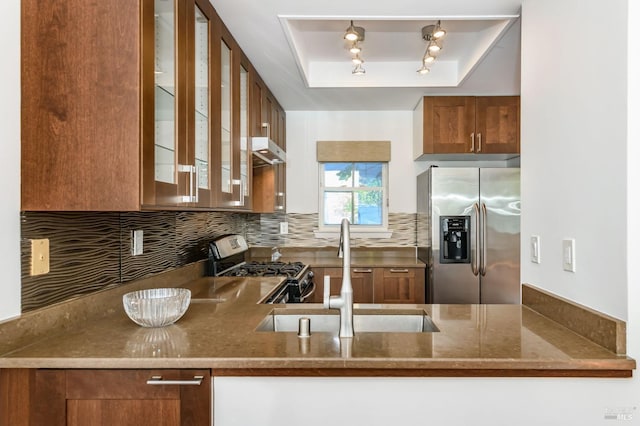 kitchen featuring a sink, appliances with stainless steel finishes, decorative backsplash, a raised ceiling, and glass insert cabinets