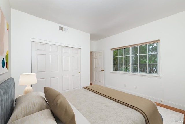 bedroom with a closet, wood finished floors, visible vents, and baseboards