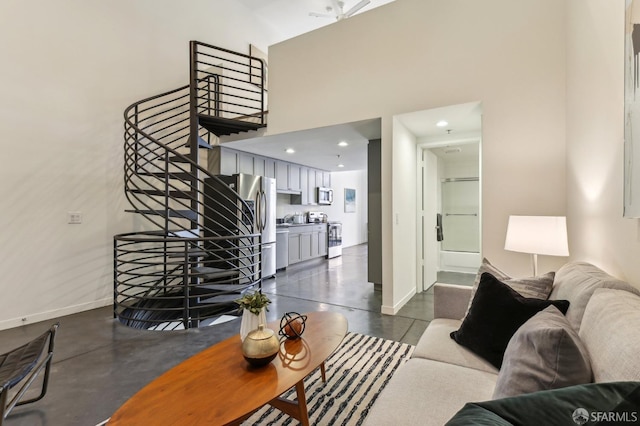 living area with concrete flooring, baseboards, stairway, and a towering ceiling