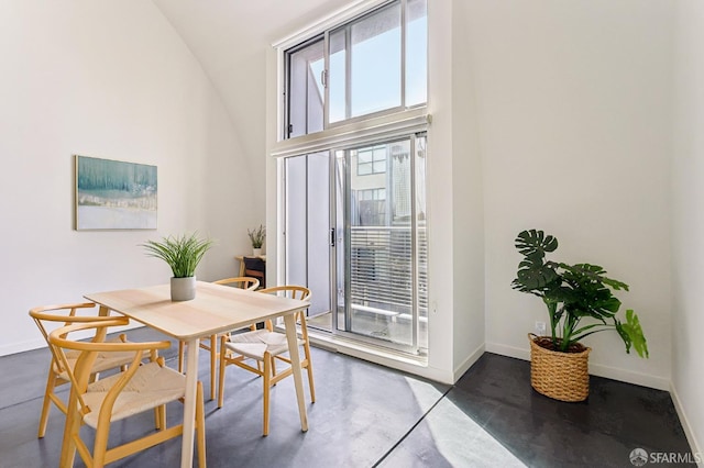 dining area featuring finished concrete flooring, baseboards, and high vaulted ceiling
