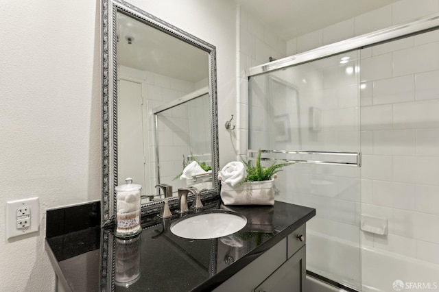 full bathroom with a textured wall, bath / shower combo with glass door, and vanity