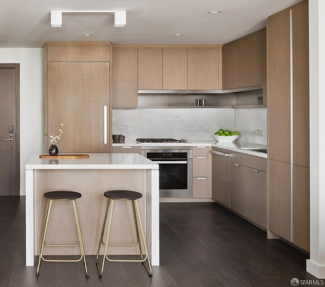 kitchen featuring light brown cabinetry, a breakfast bar area, stainless steel appliances, and dark hardwood / wood-style flooring