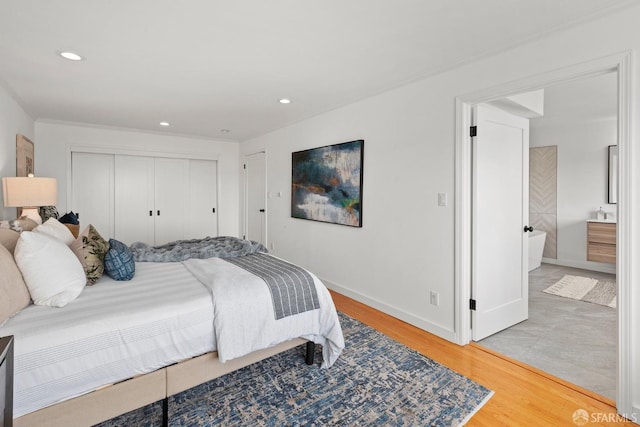 bedroom featuring a closet, light wood finished floors, baseboards, recessed lighting, and ensuite bath