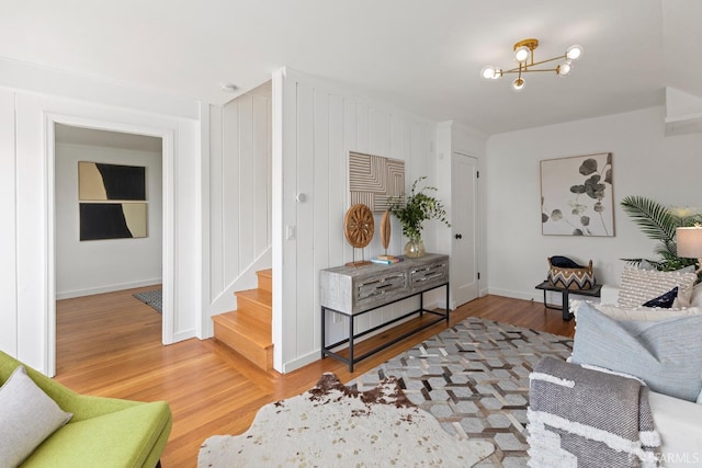 living room featuring light wood finished floors, stairway, baseboards, and a chandelier
