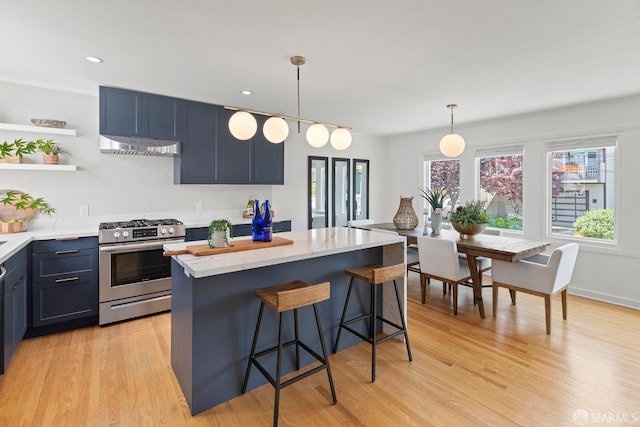 kitchen featuring gas stove, under cabinet range hood, a kitchen island, light wood finished floors, and a kitchen bar