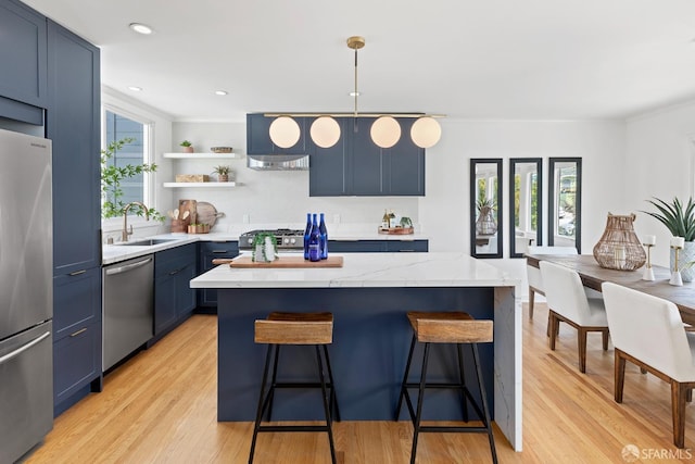 kitchen featuring stainless steel appliances, blue cabinets, a sink, a breakfast bar, and light wood finished floors