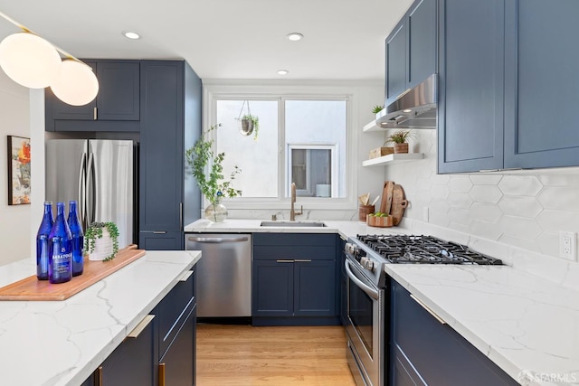 kitchen featuring appliances with stainless steel finishes, a sink, under cabinet range hood, light stone countertops, and light wood-style floors