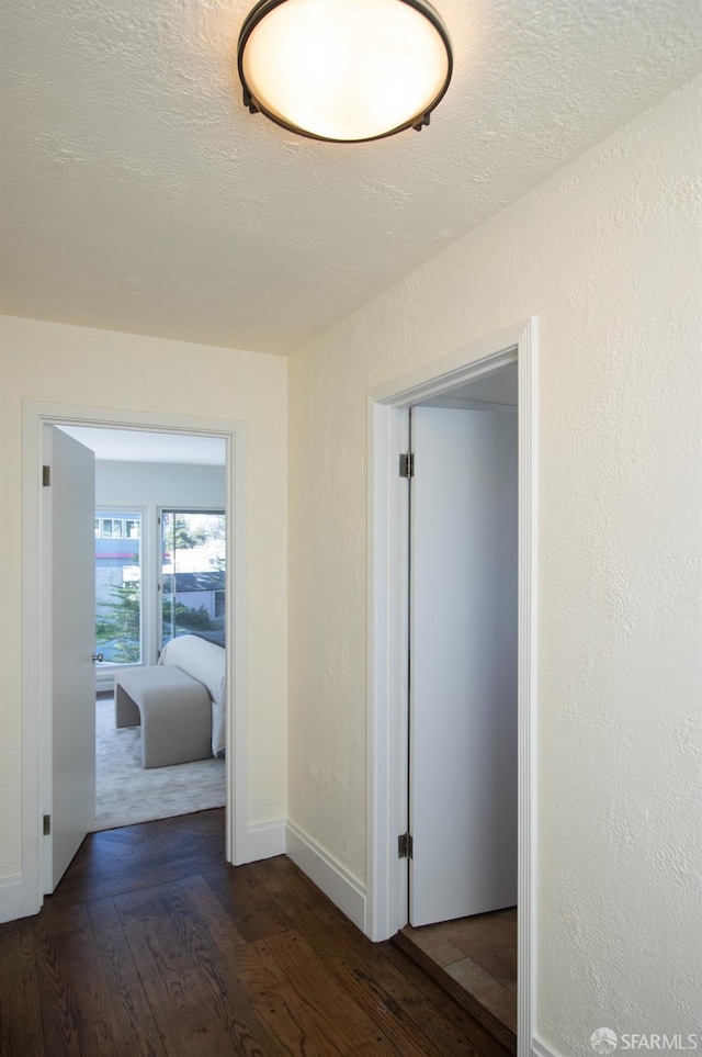 corridor with a textured wall, a textured ceiling, baseboards, and hardwood / wood-style flooring