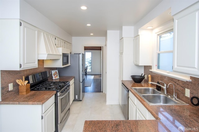 kitchen with white cabinetry, range hood, appliances with stainless steel finishes, and a sink