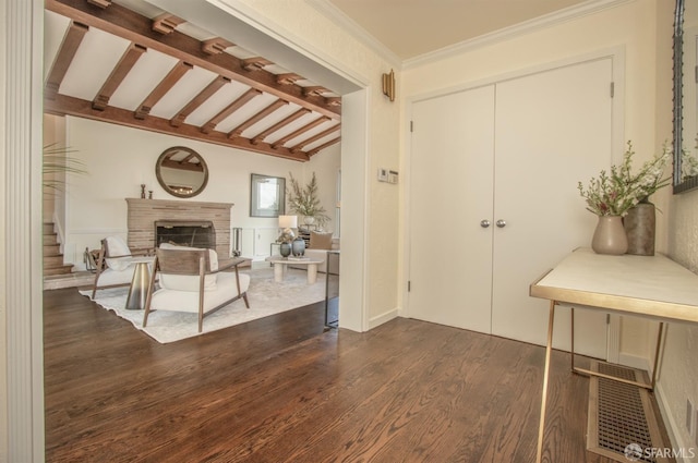 entryway with a fireplace with raised hearth, lofted ceiling with beams, ornamental molding, and dark wood-style flooring