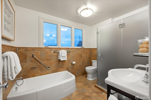 bathroom featuring toilet, tile walls, wainscoting, a bath, and a shower with door