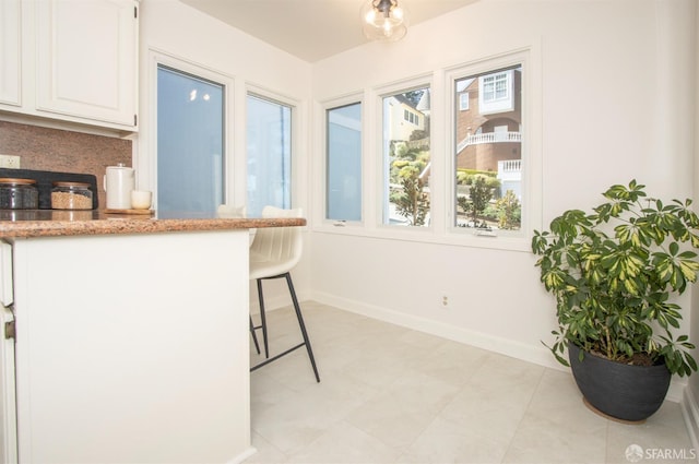 kitchen with baseboards, white cabinetry, a breakfast bar, and light stone counters