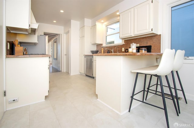 kitchen with a peninsula, white cabinetry, a kitchen breakfast bar, decorative backsplash, and dishwasher