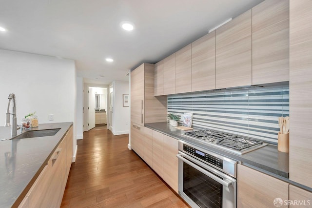 kitchen with stainless steel appliances, decorative backsplash, light brown cabinets, light hardwood / wood-style flooring, and sink