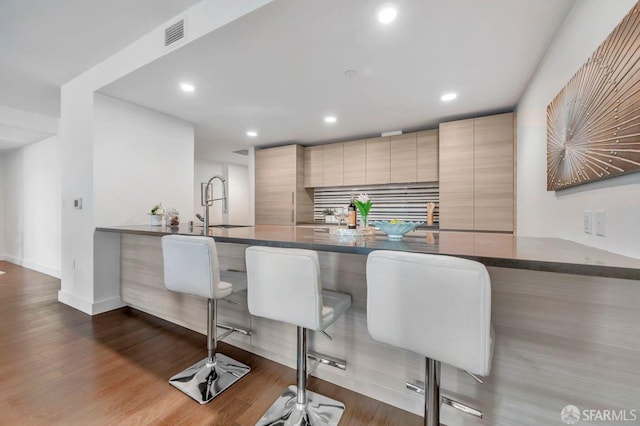 kitchen featuring hardwood / wood-style floors, light brown cabinets, sink, kitchen peninsula, and a breakfast bar area