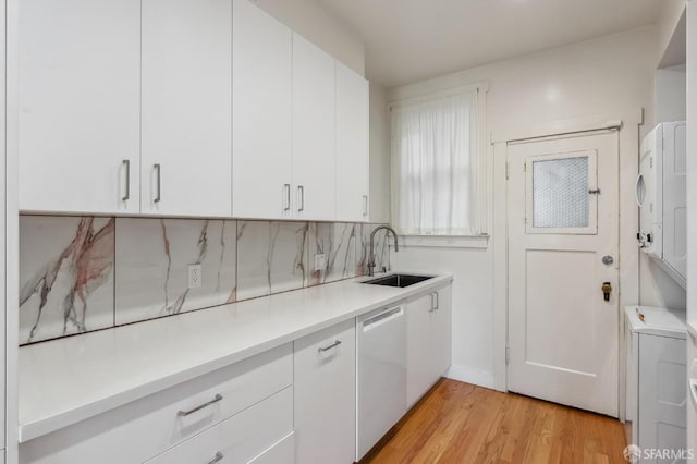 kitchen featuring white cabinets, light countertops, white dishwasher, and a sink