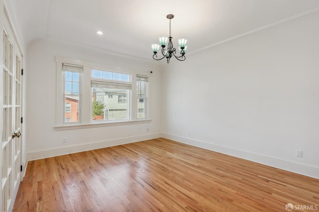 spare room with ornamental molding, a notable chandelier, light wood-style flooring, and baseboards