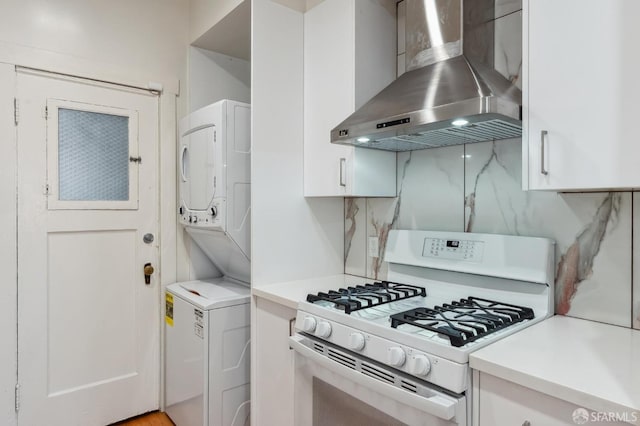 kitchen featuring white gas stove, extractor fan, white cabinets, light countertops, and stacked washer and clothes dryer