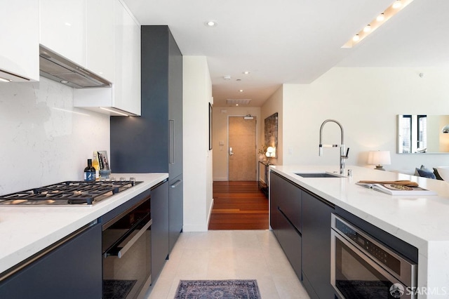 kitchen featuring light hardwood / wood-style flooring, range hood, sink, white cabinets, and appliances with stainless steel finishes