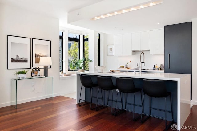 kitchen with a breakfast bar area, sink, dark wood-type flooring, and white cabinetry