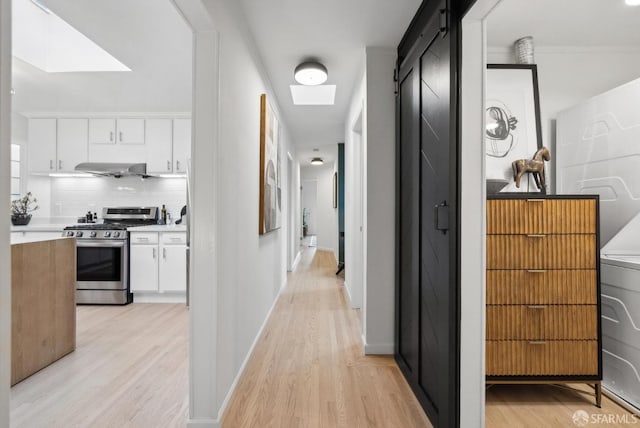 corridor featuring baseboards, washer / dryer, a skylight, and light wood finished floors