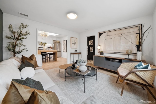 living area with a notable chandelier, visible vents, and light wood-type flooring