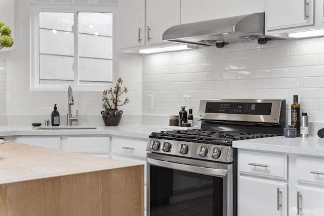 kitchen with gas range, white cabinets, wall chimney exhaust hood, and a sink